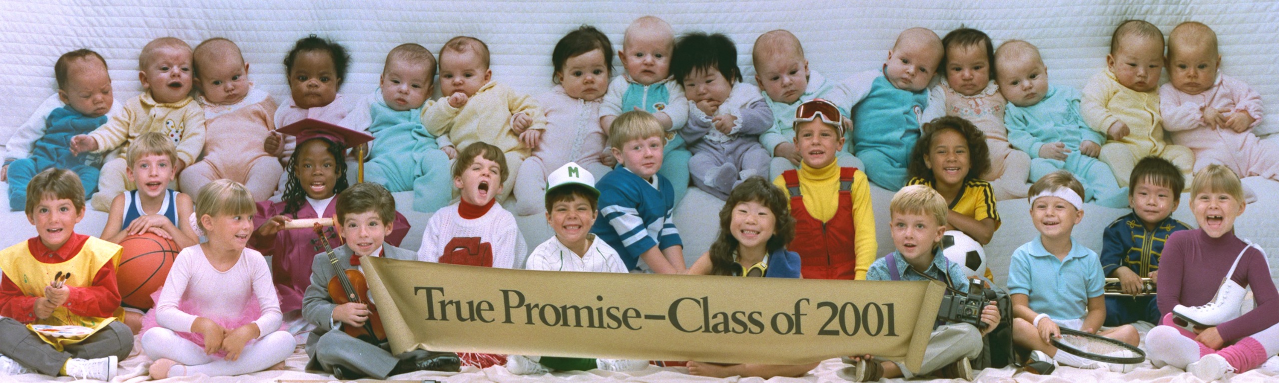 A row of babies in pastel sleepsuits sits on a quilted backdrop above a row of laughing children dressed as a painter, ballerina, violinist, baseball player, skier, tennis player and more, holding a banner reading &ldquo;True Promise &ndash; Class of 2001&rdquo;.