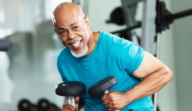A man holds a pair of heavy dumbbells and smiles at the camera.