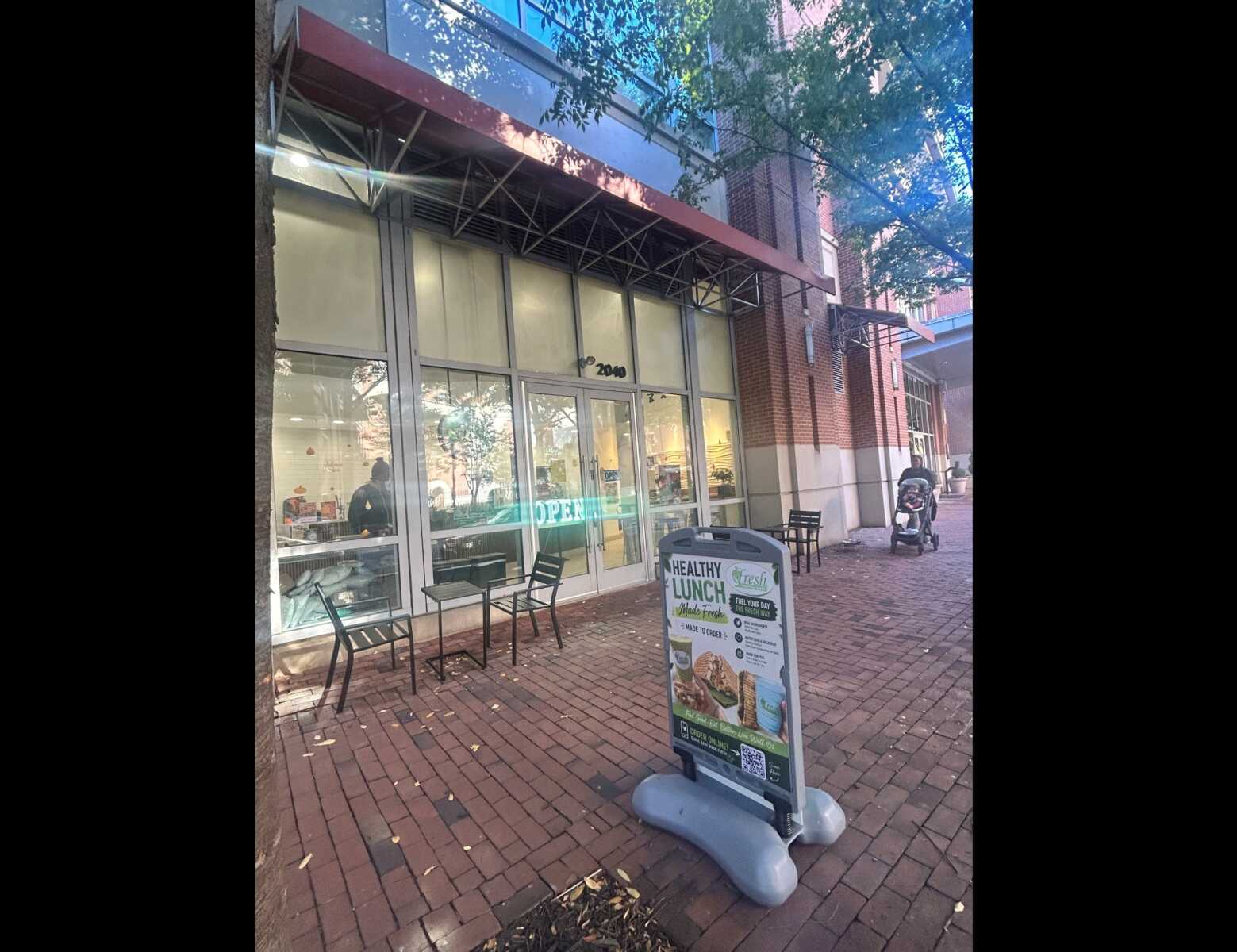 Cafe storefront with large glass doors, red awning, and outdoor tables on a brick sidewalk; a menu sign outside.