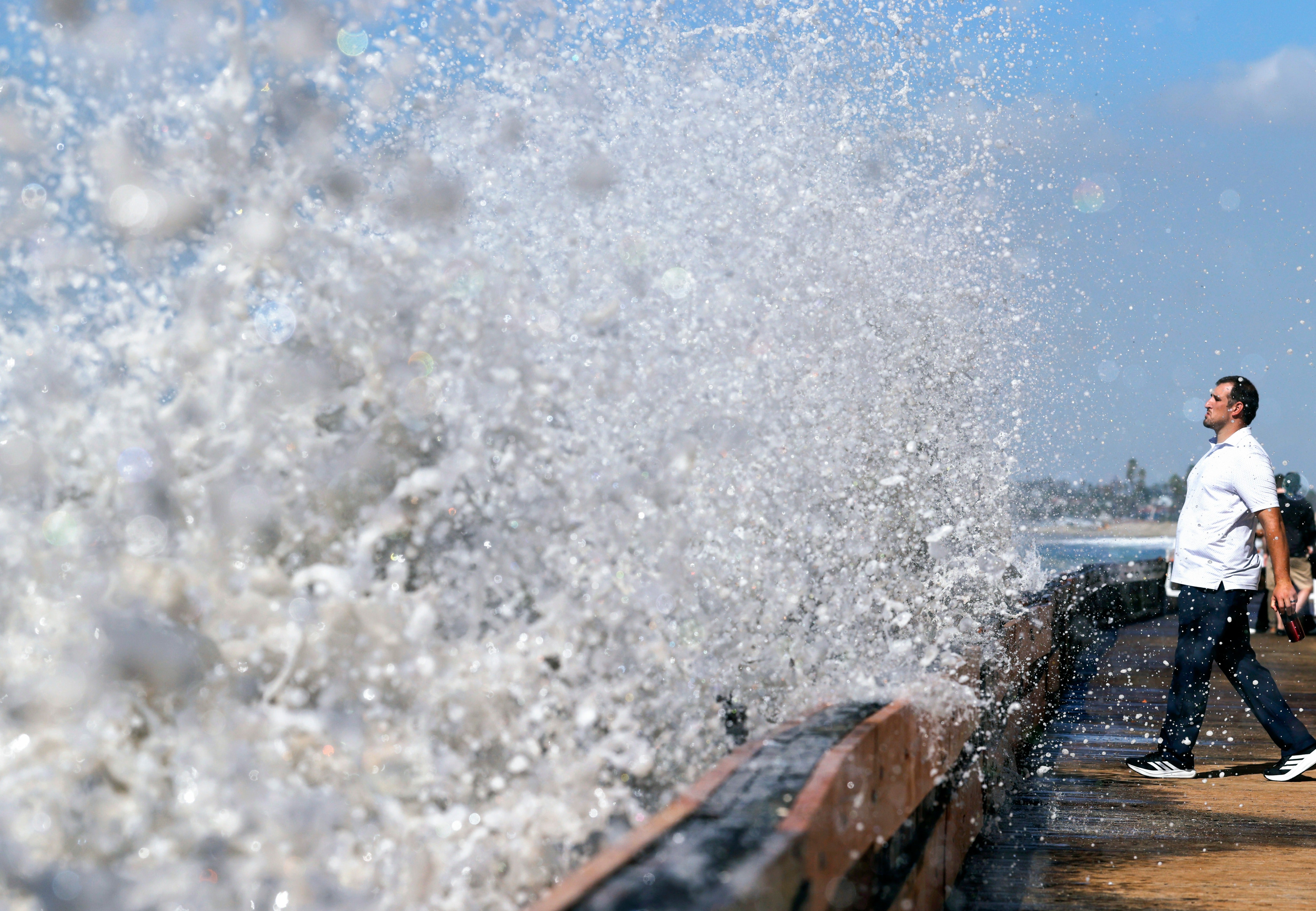 A person watches as a Pacific Ocean wave crashes into a seawall protecting beachfront homes in Long Beach, California, on Monday. The remnants of Pacific Hurricane Polo are bringing widespread flooding threats through the weekend
