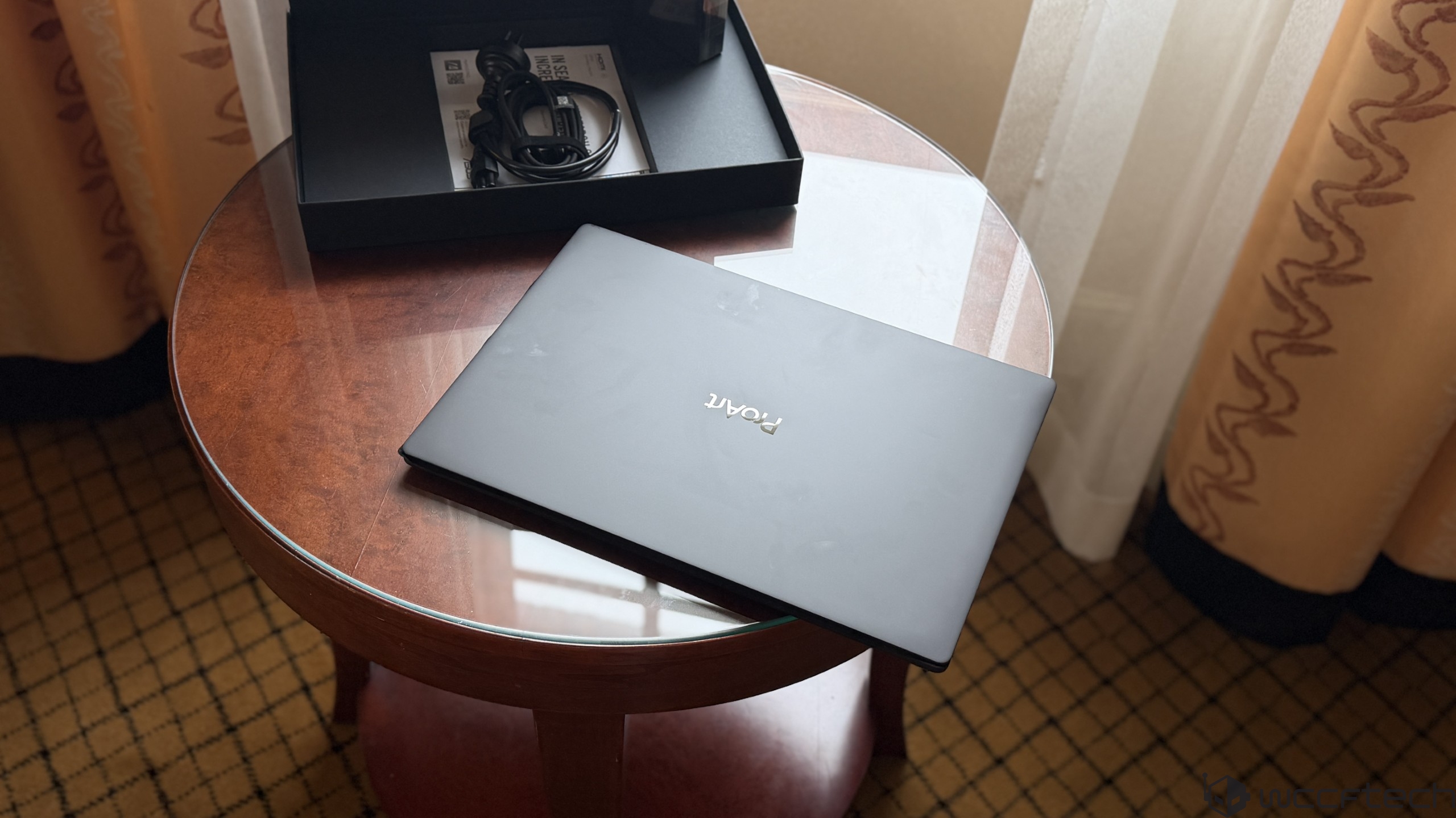 A laptop with the 'PORTÉ' logo is placed on a round wooden table next to its open box containing cables and a manual.