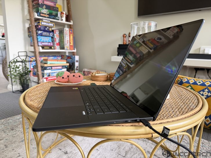 A Razer Blade laptop is placed on a round wicker table, with a background of colorful board games on a shelf.