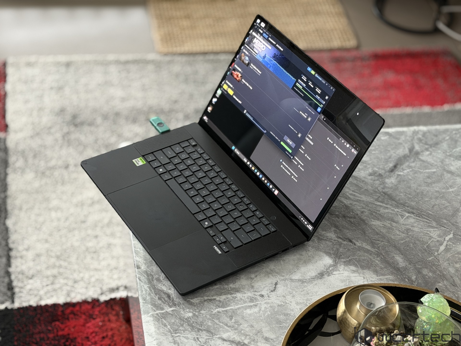 A Razer Blade laptop on a table displays the Steam interface with 'Metro Exodus' downloading.