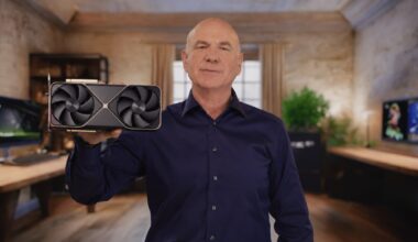 A person holds up an NVIDIA graphics card with a prominent dual-fan design in an office setting.