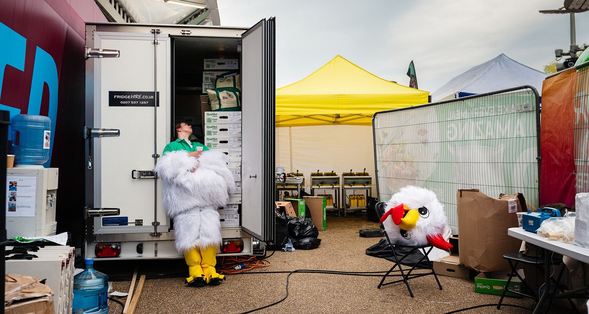 Photo titled Headless Chicken by Marc James: a performer at the World Halal Food Festival escapes the heat of their chicken costume by cooling off in a refrigeration truck, costume head on a chair.