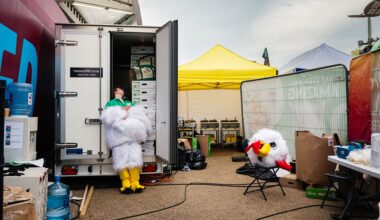 Photo titled Headless Chicken by Marc James: a performer at the World Halal Food Festival escapes the heat of their chicken costume by cooling off in a refrigeration truck, costume head on a chair.