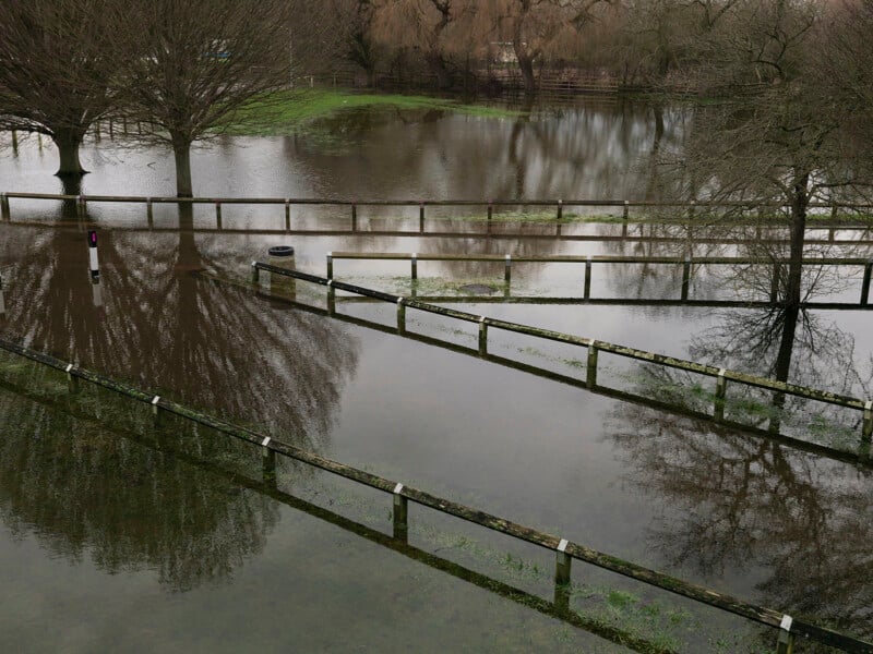 A flooded park area with bare trees and wooden fences partially submerged in standing water.
