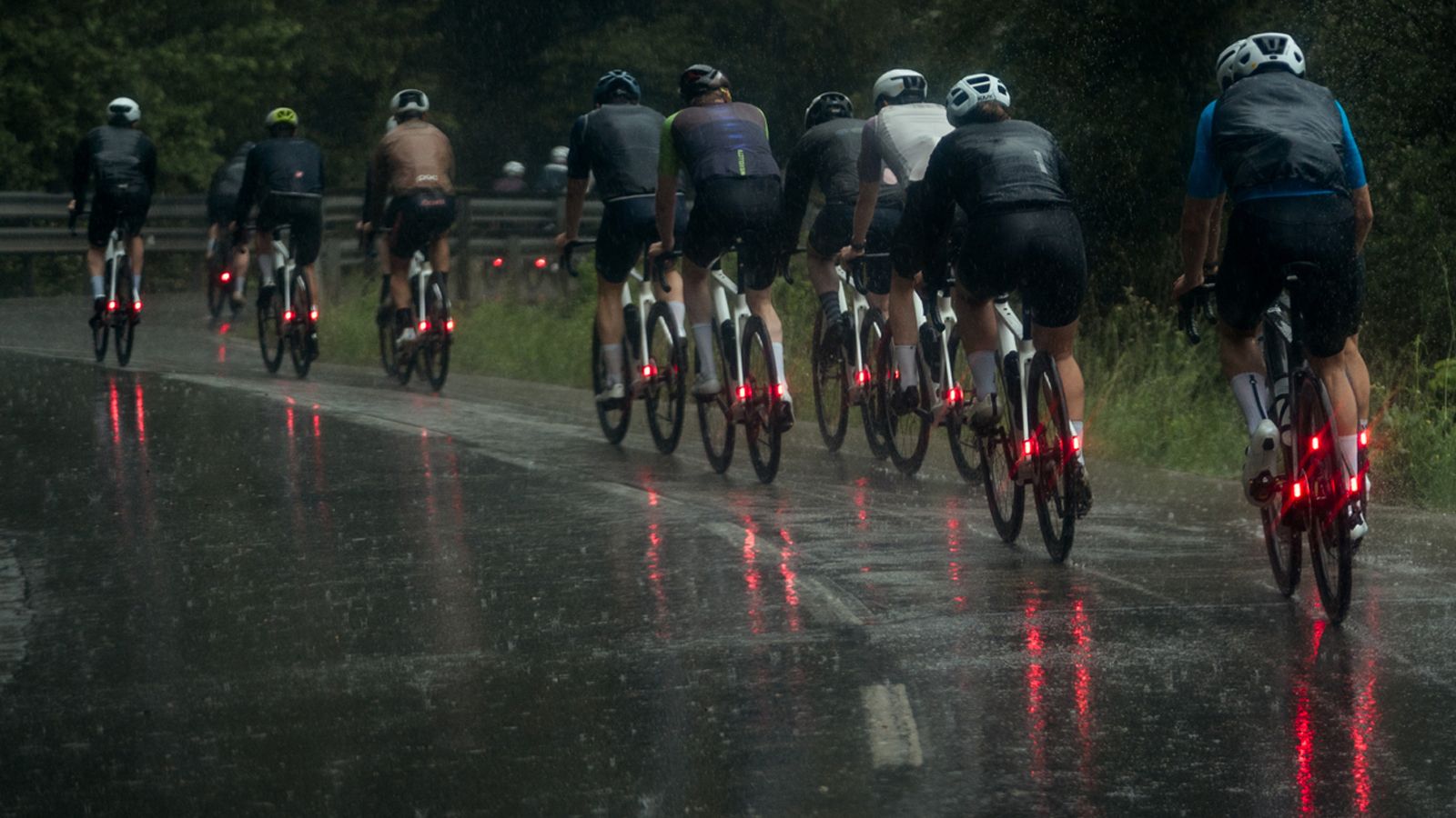 A group of cyclists cycling on a wet road in winter, each of them using winter road bike tyres and with bright red lights on the rear of their bikes