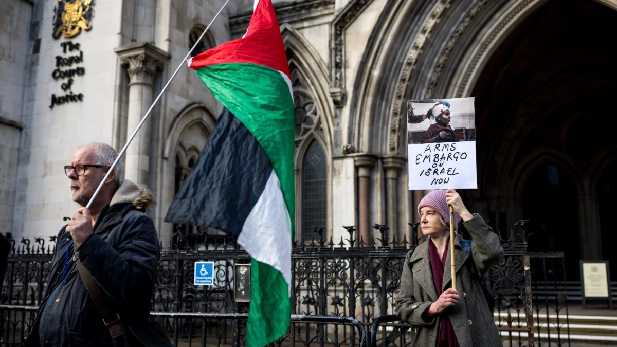 LONDON, ENGLAND - DECEMBER 2: Protesters holding a placard and a Palestinian flag gather outside the Royal Courts of Justice on December 2, 2025 in London, United Kingdom. A three-day judicial review is being heard by the High Court on the proscription of Palestine Action (PA) as a terrorist group. PA co-founder Huda Ammori leads the challenge to the pro-Palestinian campaign group's proscription under the Terrorism Act 2000. Last month the Home Office lost an appeal to block the review, which was due to begin on November 25, but was postponed a day. The Home Office-imposed ban on membership or support of PA took effect on July 5, after activists from the pro-Palestinian group broke into RAF Brize Norton and spray-painted two Voyager aircraft. Since their proscription, more than 2,000 people have been arrested for allegedly showing support of PA, mostly while holding signs reading: "I oppose genocide, I support Palestine Action." (Photo by Jack Taylor/Getty Images)