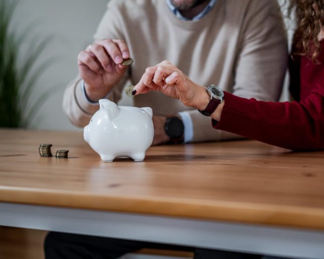 Couple dropping coins into a white piggy bank, planning household savings and budgeting together for future security and retirement