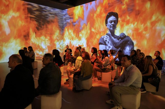 Visitors watch a projection, at the exhibition 