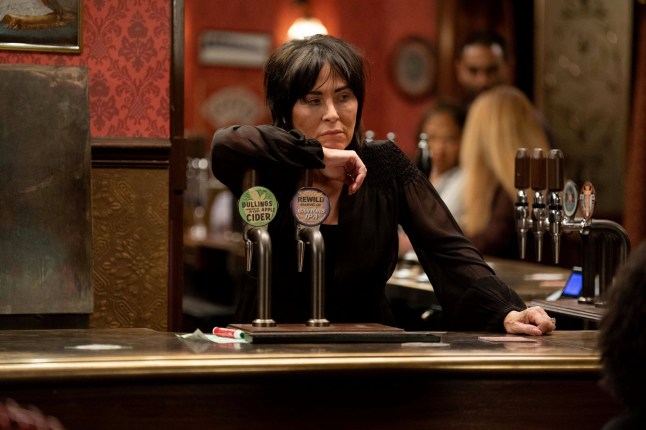 Kat Moon leaning on the taps at the bar in EastEnders, looking serious and upset.
