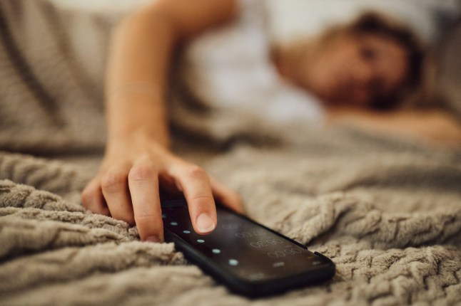 Close up of unrecognizable woman turning off her alarm clock on cell phone on a bed.