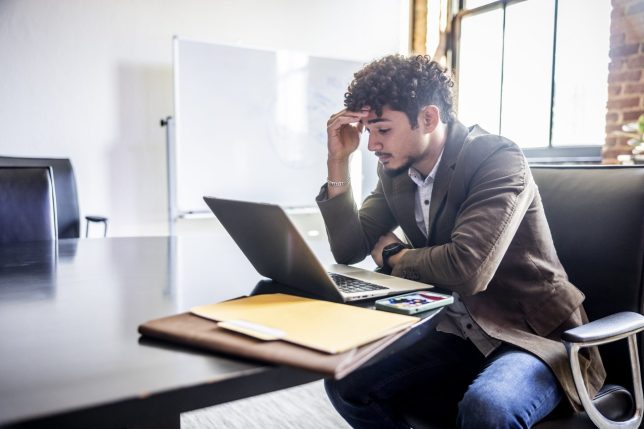 Young businessman working on laptop and looking worried in modern office conference room