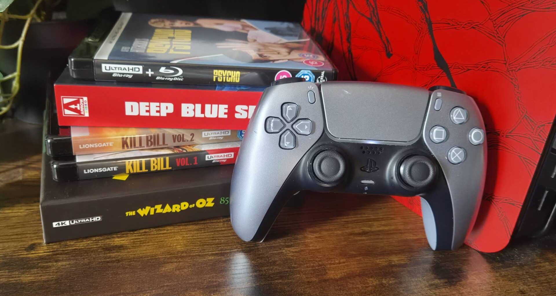Photo of a silver PS5 DualSense controller sitting next to a pile of 4K Blu-rays.