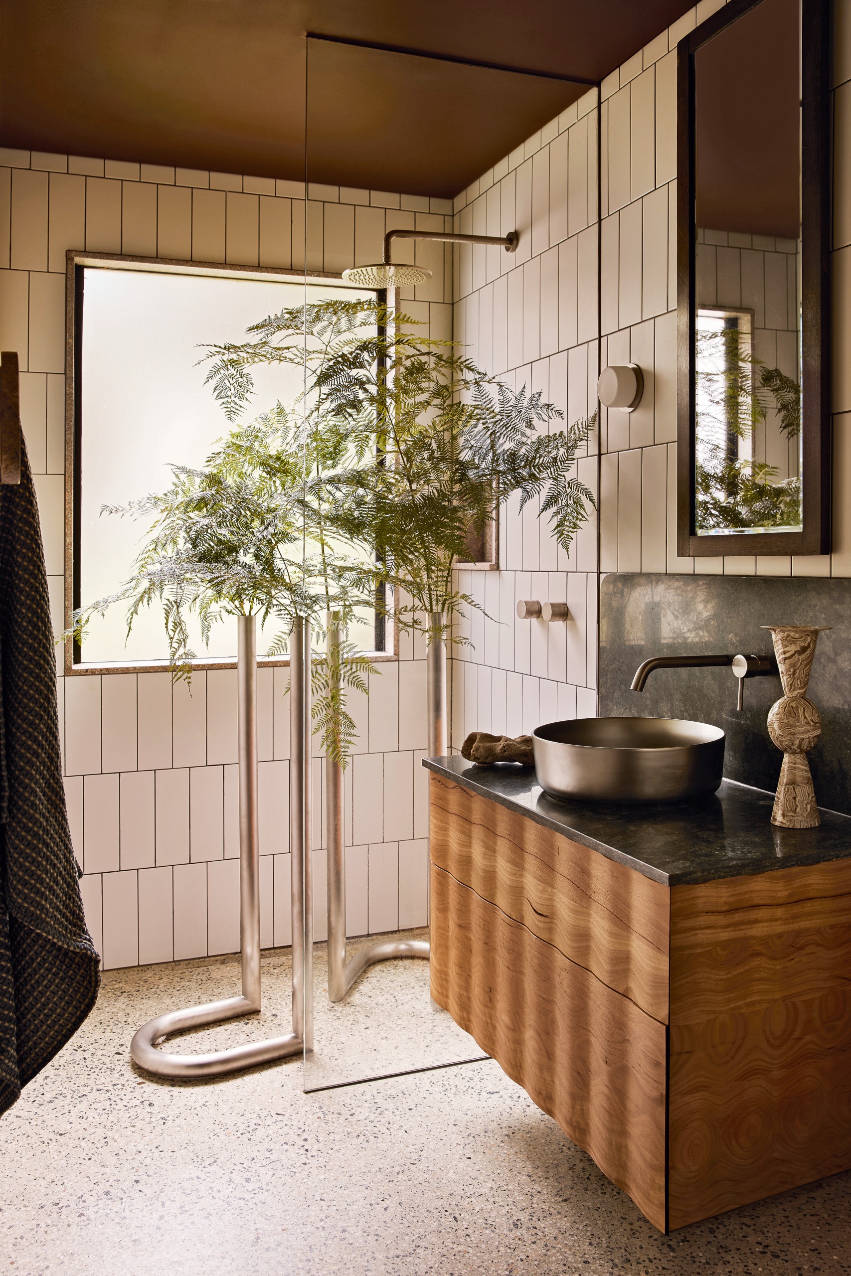 Bathroom with white metro tiled walls, brown painted ceiling, white terrazzo floor and wavy wood vanity