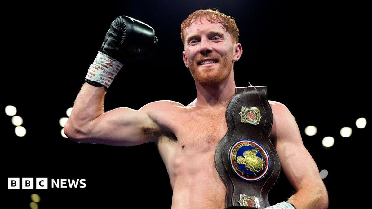 Bowen has red hair and a red beard. He is standing with his right hand raised and the Midlands title belt over his left shoulder.