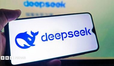 A hand holds a mobile phone, displaying the Blue deepseek logo of a blue cartoonish whale on a white background.