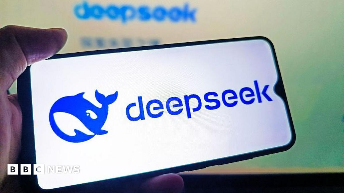 A hand holds a mobile phone, displaying the Blue deepseek logo of a blue cartoonish whale on a white background.