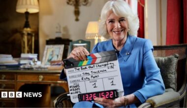 Queen Camilla sits in a chair reading a copy of William Boyd's Restless