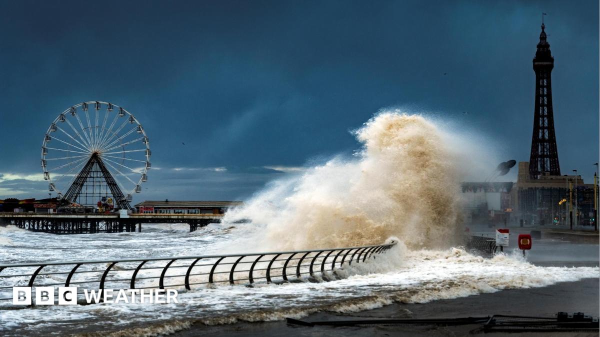 Large waves crash onto the promenade at Blackpool. Blackpool Tower and a ferris wheel are in the background.
