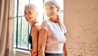 Two women in their 50s smiling back to back in a light airy studio