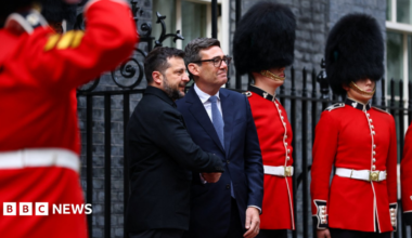 MI5 chief Sir Ken McCallum has short dark hair, dark glasses and is wearing a dark suit with a green tie.