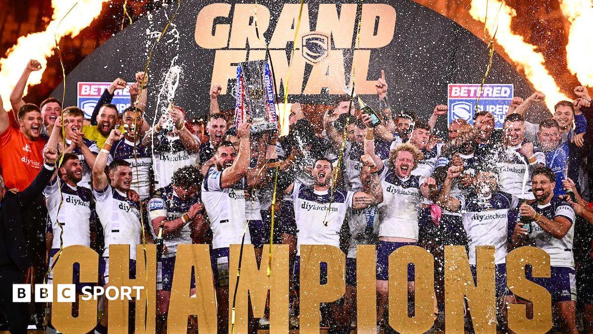 Wakefield lift the Super League trophy with 'CHAMPIONS' in front of them and a big gold GRAND FINAL arch behind them