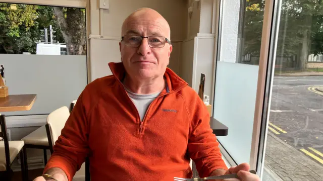 A man with glasses wearing an orange 1/4 zip