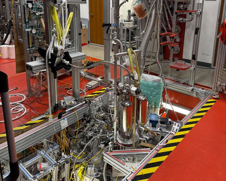 Cyclotron set-up in a laboratory showing metal pipes, tanks and wires in a recess in the floor.