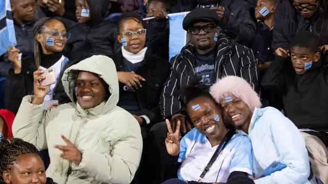 Botswana supporters smile, wave flags and pose for photos, many with di national flag painted on dia cheeks