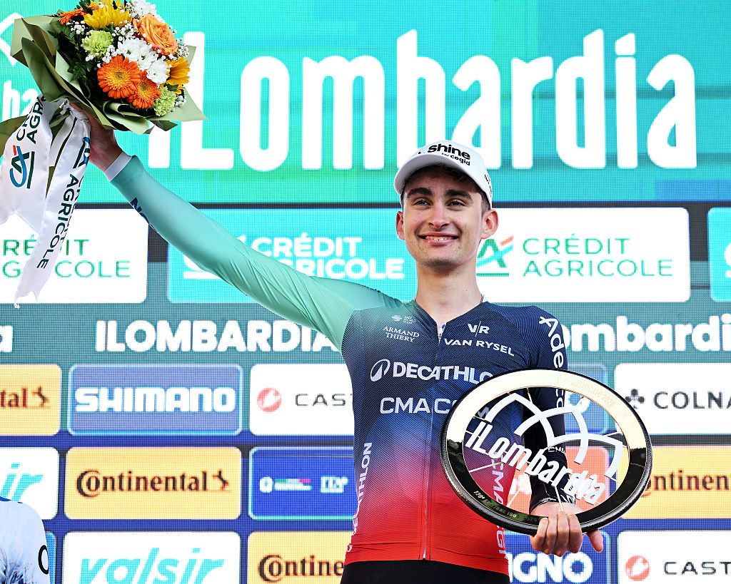 Seixas holding up the bouquet of flowers and trophy on the Lombardia podium