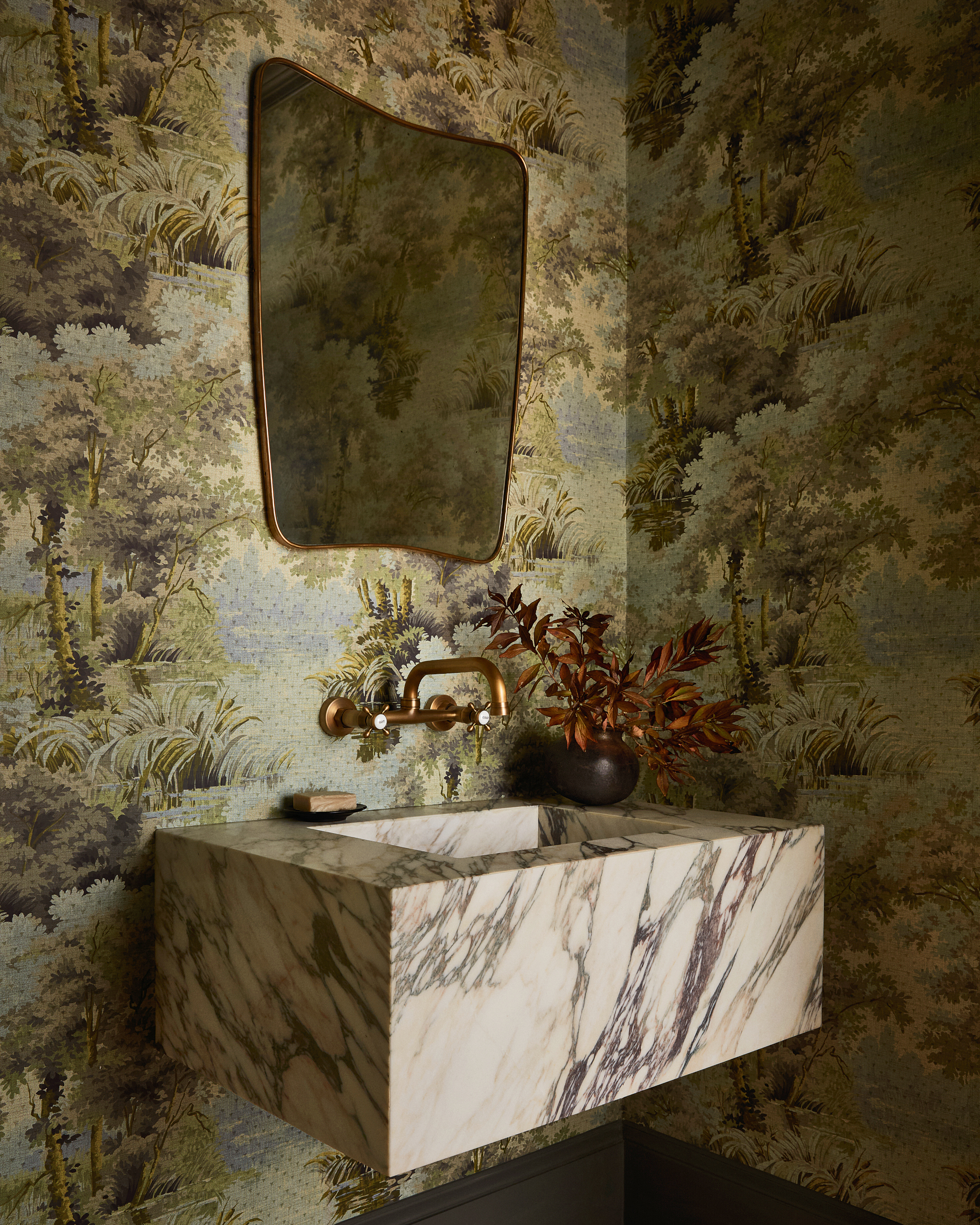 Powder room with green botanical wallpaper, floating wall sink with white marble, and brass wall tap