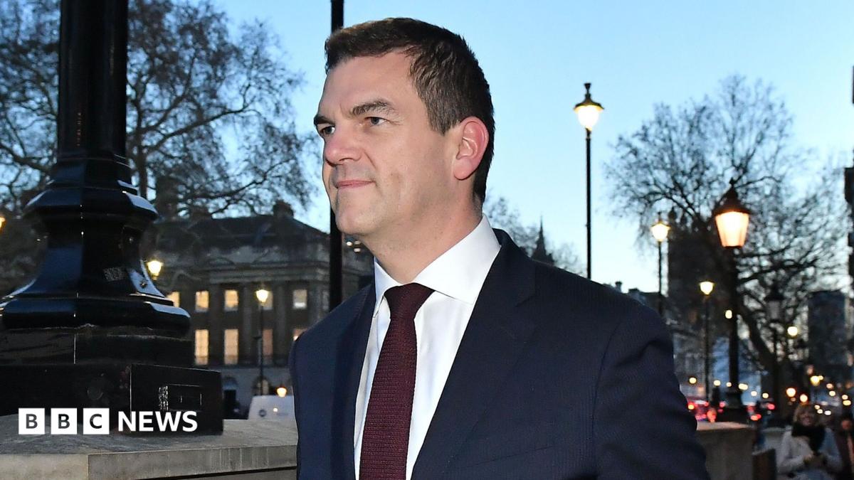 Sir Olly Robbins walking down Whitehall wearing a suit and tie.