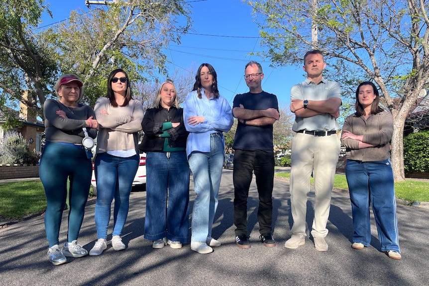 A group of residents stand across a road with their arms folded.