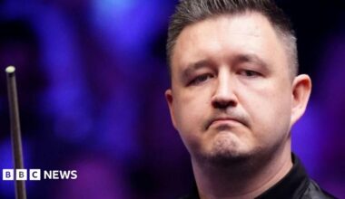 Kyren Wilson looking off camera holding a snooker cue.