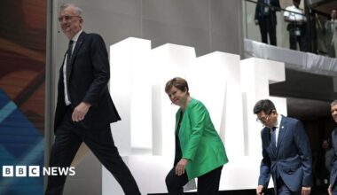 Three people walking up stairs one behind each other against a backdrop of white letters spelling IMF.