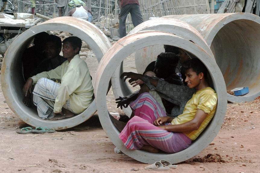Bangladeshi labourers rest inside large concrete pipes.
