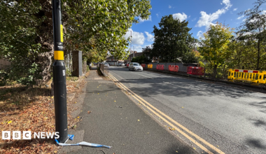 Some railings either side of a road with a lamp-post on the left in the foreground. The remains of some police tape are tied to the base of the lamp-post