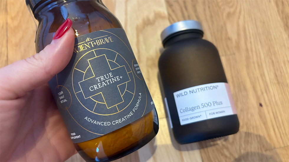 Supplement stacking hand holding jar of creatine next to collagen jar on wooden surface
