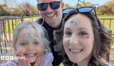 Pictured is Seren, Mark and Clare. Seren has a unicorn headband on, and gems on her face. She is smiling at the camera. She has a purple top on. In the middle, is her dad Mark. He is smiling at the camera and wearing black sunglasses. He has a black top on too. To the right of the photo, is Seren's mum, Clare. She has gems on her face too. She has a green unicorn headband on. She is smiling at the camera, and has curly brown hair.