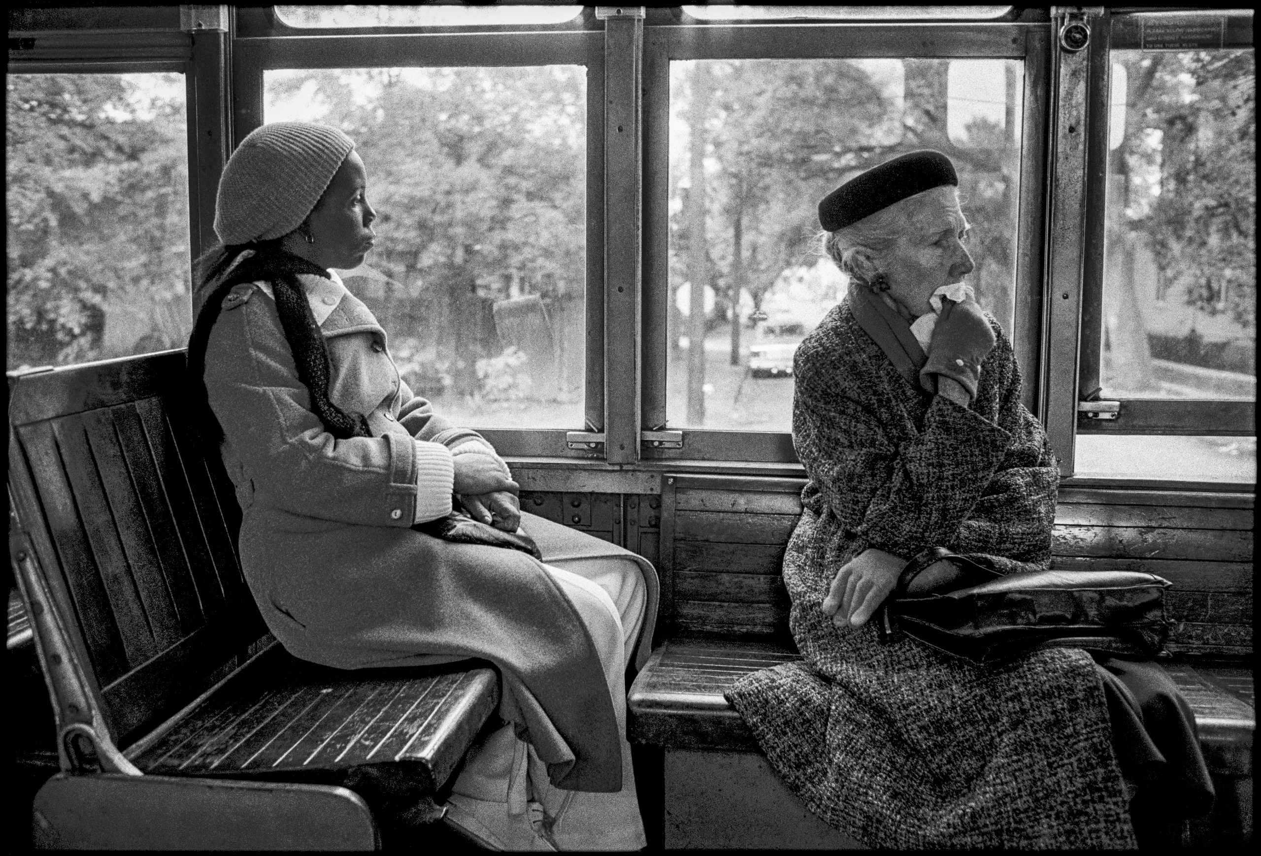 A black-and-white photograph showing two women sitting on a public transit vehicle, looking out the large side windows.