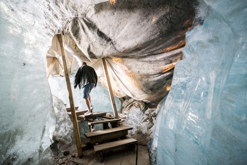The back of a man walking through ice. Woolen blankets are attached to some of the ice.