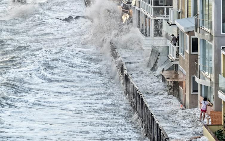 Water laps up against homes along the coast, including inside a temporary barrier created to protect them.