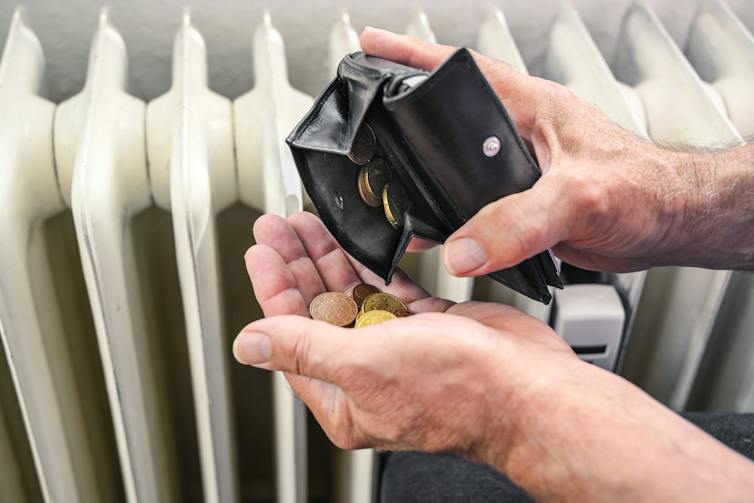 An elderly person counting coins from a wallet in front of a radiator