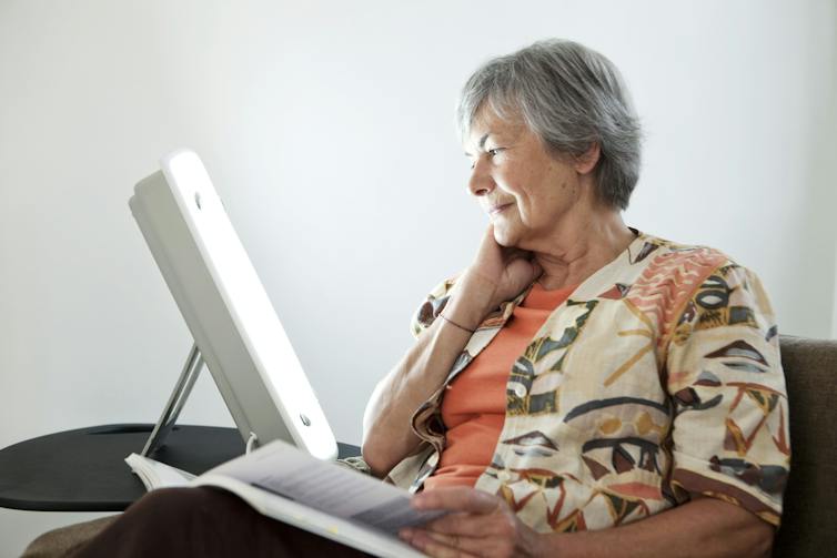 Woman reads book while sitting in front of an SAD lamp