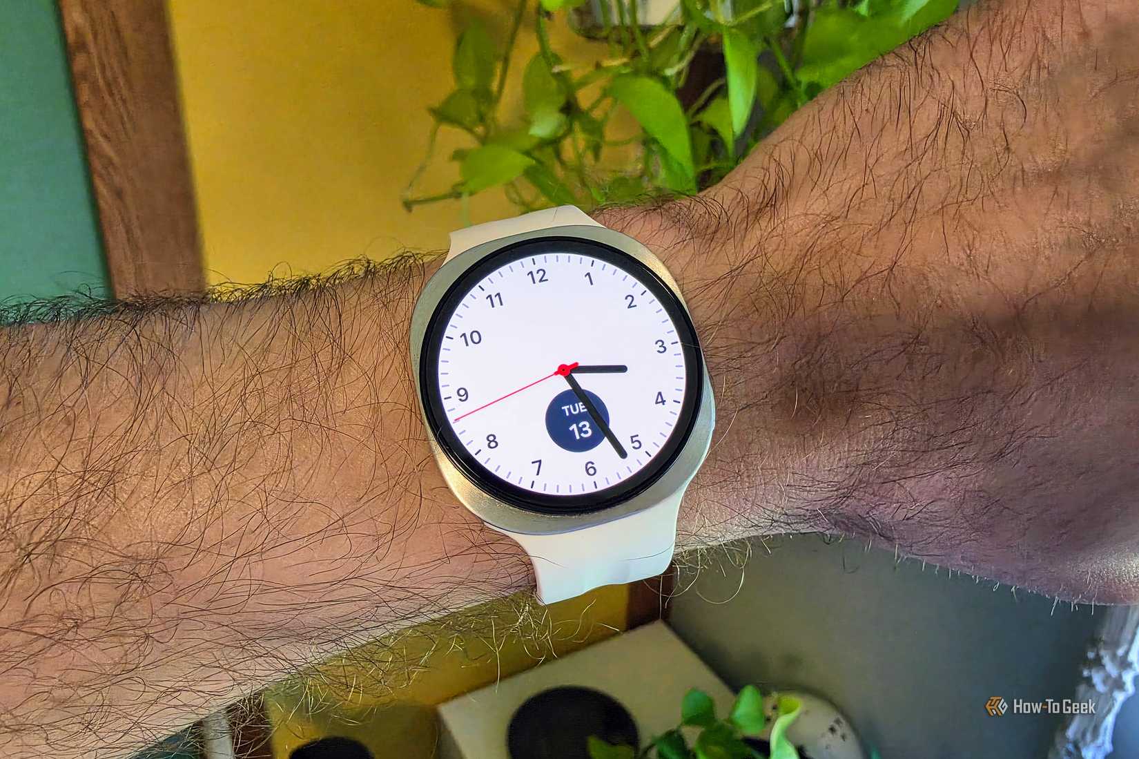 Samsung Galaxy smartwatch with a white strap and an analogue watch face displaying the time, worn on a person's wrist.