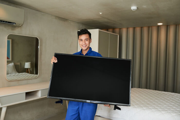 A man holding a flat-screen television in a bedroom, representing valuable dumpster finds.