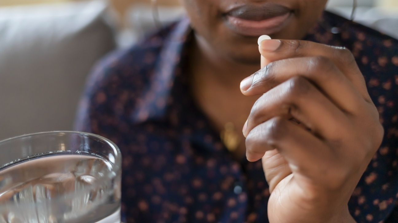 Female taking a small white pill with a glass of water