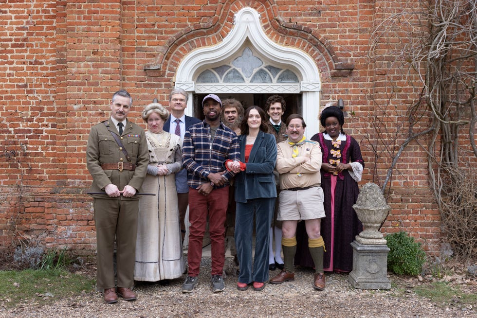 Ghosts series 5 full cast outside Button House in a scene from ghosts series 5, a group of people dressed in clothes from different time periods stand outside the doorway of a stately home